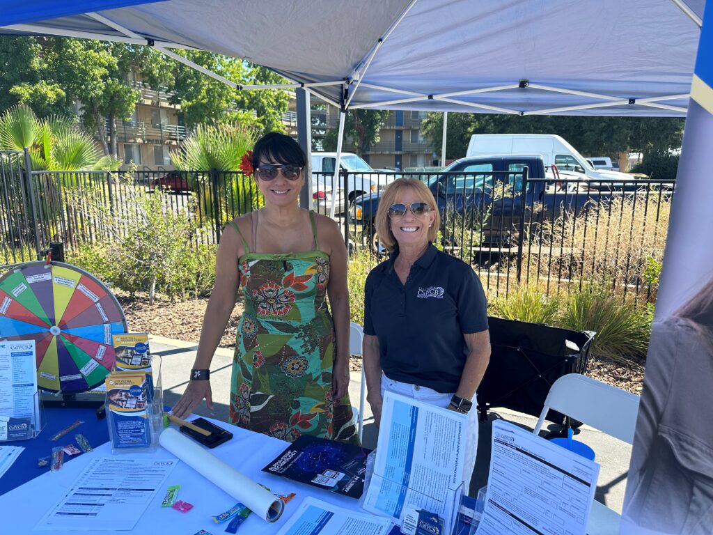 Two women behind an informational booth smiling.